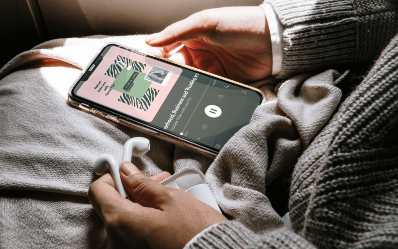 a woman in a grey jumper hold a phone in her lap. On the phone is a preview of Holly's interview on the Lioness Tribe podcast, where she speaks about Confidence, Motherhood and Entrepreneurship